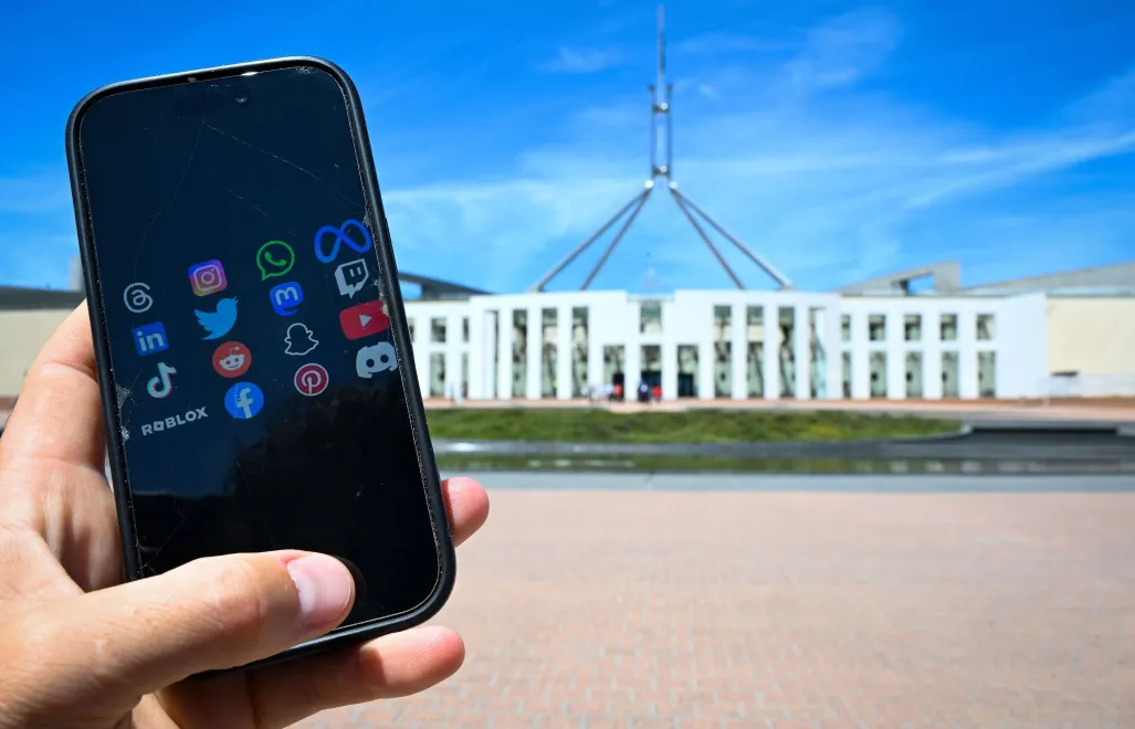 Smartfon z aplikacjami social mediów na tle parlamentu w Canberze Fot. PAP/EPA/LUKAS COCH