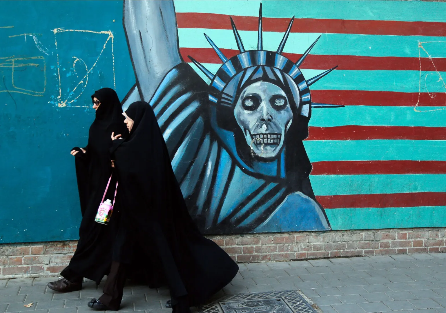 Zdjęcie archiwalne z 3 listopada 2016 r. przedstawia Iranki przechodzące obok antyamerykańskiego muralu w drodze do byłej ambasady USA w Teheranie Fot. PAP/EPA/ABEDIN TAHERKENAREH