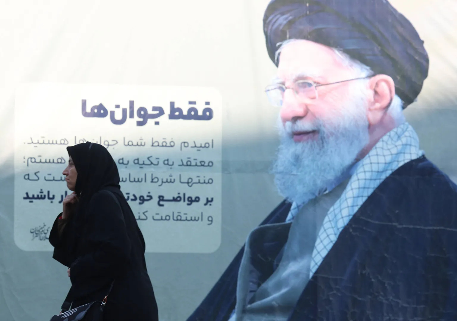 Женщина в чадре идет мимо плаката с изображением верховного лидера Ирана аятоллы Али Хаменеи на церемонию памяти погибших в антиправительственных протестах в Иране. Тегеран, Исламская Республика Иран. 17 февраля 2026 года. Fot. PAP/EPA/ABEDIN TAHERKENAREH